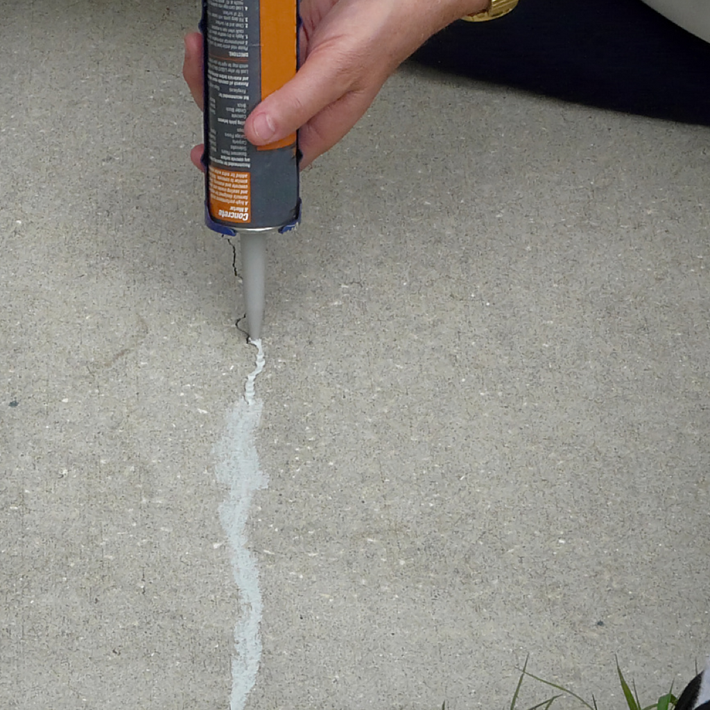 A concrete service technician uses a caulk gun to seal a crack in concrete with caulk.