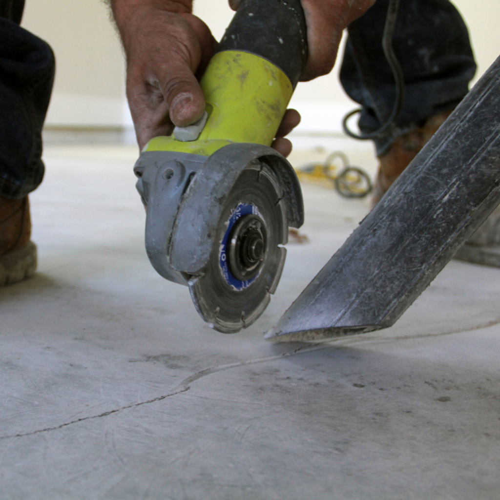 A service technician uses a concrete grinder to clean and a vacuum to absorb the dust created in preparation for concrete crack repair.