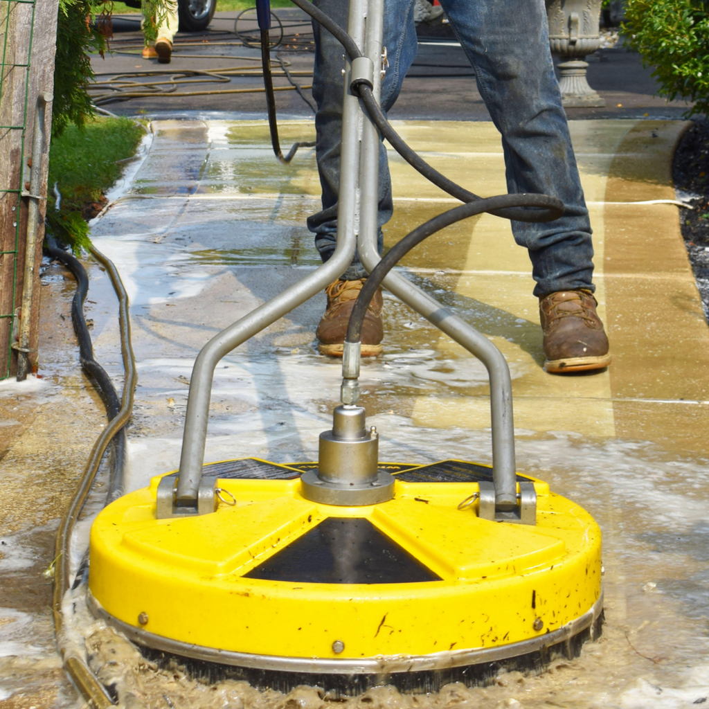 A technician uses a concrete scrubbing machine to clean a dirtied front walkway.
